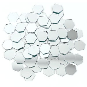 Puede incluir: Un montón grande de azulejos de espejo hexagonales plateados. Los azulejos están dispersos sobre un fondo blanco.