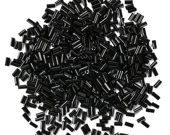 May include: A large pile of black glass seed beads. The beads are small and cylindrical in shape.