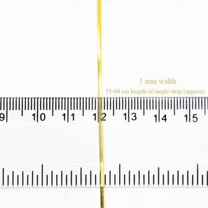 May include: A close-up of a gold ribbon measuring 1 mm wide and 55-60 cm long. The ribbon is placed on a ruler for size reference.