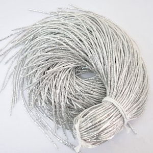 May include: A bundle of silver metallic cord, approximately 91 metres long, is tightly wound and ready for crafting projects.