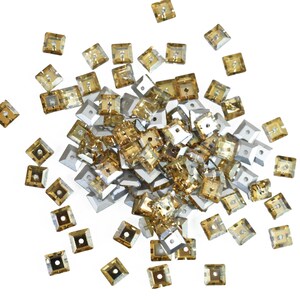 May include: A collection of square, amber-coloured rhinestones with a metallic silver backing. Each rhinestone has a small square hole in the centre. The rhinestones are scattered on a white background.