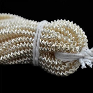 May include: A close-up of a bundle of gold-colored, metallic, zig-zag trim. The trim is tied together with a white string.