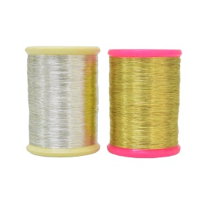 May include: Two spools of metallic thread, one silver and one gold, on a white background.