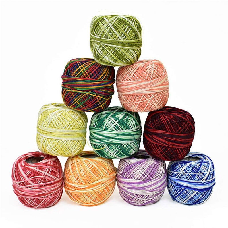May include: A pyramid of colorful embroidery thread balls. The threads are in various colors, including green, red, yellow, orange, purple, and blue. The balls are tightly wound and appear to be made of cotton or a similar material. Ideal for embroidery and other crafts.