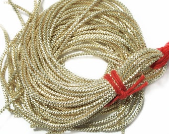 May include: A spool of gold metallic cord, wound tightly, with a red thread tied around the center.
