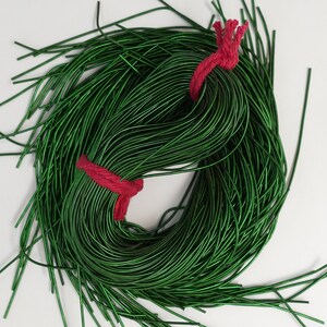 May include: A spool of green metallic wire tied with a red string. The wire is thin and shiny, and the spool is full of wire.
