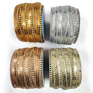 May include: Four spools of decorative sequin trim in gold, silver, and bronze tones. The trim is tightly wound on blue spools, with the sequins arranged in vertical rows. The sequins catch the light, creating a shimmering effect, perfect for embellishments.