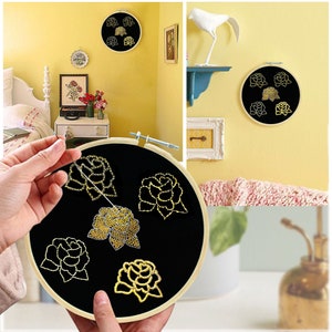 May include: A close-up of a black embroidery hoop with gold embroidery of roses. The hoop is being held by a hand and the needle is being threaded through the fabric.