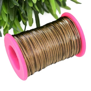 Pode incluir: Uma bobina de cordão metálico dourado e preto com uma bobina de plástico rosa.