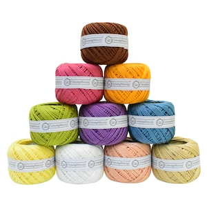Puede incluir: Una colección de diez carretes de hilo de bordar en varios colores, incluyendo marrón, rosa, amarillo, verde, morado, azul, blanco, melocotón y beige. Cada carrete está envuelto con una etiqueta blanca que dice "Embroidery Material".