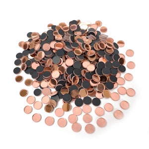 May include: A collection of small, circular embellishments in rose gold, black, and silver. The shiny, flat discs are scattered on a white surface, creating a textured effect. Suitable for craft projects, these are ideal for adding detail.