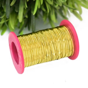 May include: A spool of gold-colored wire with a pink plastic casing. The wire is wound tightly around the spool.