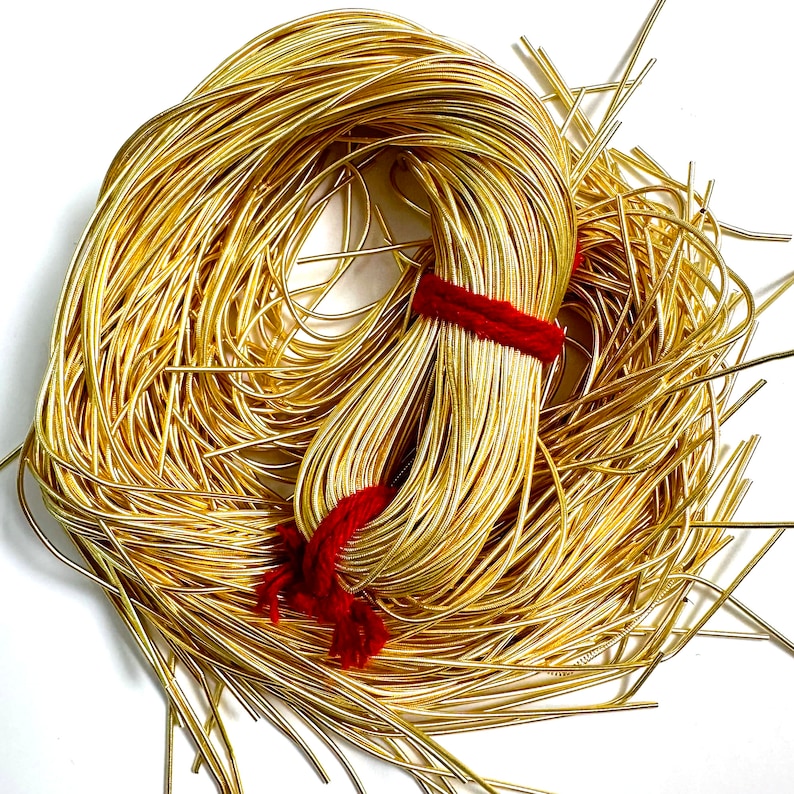 May include: A large spool of gold-colored wire, tied with a red string. The wire is thin and flexible, and it is perfect for crafting jewelry or other projects.