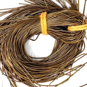 Op de afbeelding: Een bundel goudkleurig draad, gebonden met een beige touwtje. De draad is in een cirkel gewikkeld, met de uiteinden van de draad die eruit steken.