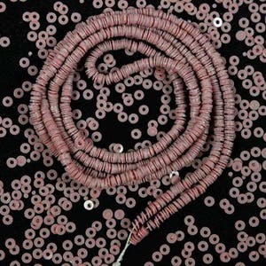 Op de afbeelding: Een streng roze ronde kralen, gemaakt van keramiek of glas, met een matte afwerking. De kralen zijn in een cirkelvormige patroon gerangschikt, waardoor een decoratief effect ontstaat. De kralen zijn verspreid over een zwarte achtergrond.