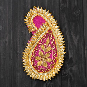 May include: A pink paisley-shaped fabric patch with gold embroidery and beading. The patch is surrounded by a gold trim with a scalloped edge.