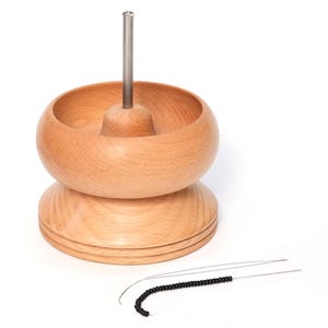 Puede incluir: Una bandeja de abalorios de madera con una varilla de metal en el centro. Una hebra de cuentas negras está en un alambre al lado de la bandeja.