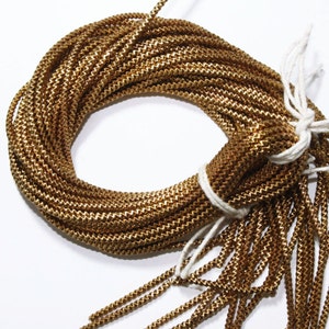 Może przedstawiać: Szpula ze złotym, plecionym sznurkiem, związana białym sznurkiem. Sznurek jest fakturowany i ma delikatny połysk.