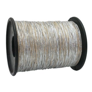 May include: A spool of metallic thread with silver and tan strands. The thread is wound around a black plastic spool. The thread has a slight sheen, reflecting light. The spool is set against a white background.