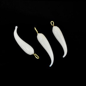 May include: Three white glass horn-shaped charms with gold-colored metal loops. The charms are hanging against a black background.