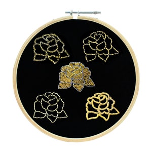 May include: Five gold embroidered roses on a black fabric background in a wooden embroidery hoop.