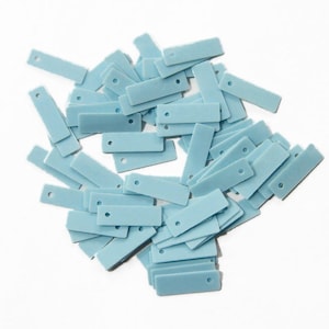 Könnte beinhalten: Ein Haufen kleiner, rechteckiger, hellblauer Etiketten mit einem einzelnen Loch an einem Ende. Die Etiketten sind auf einem weißen Hintergrund verstreut. Diese Etiketten könnten zum Beschriften oder Basteln verwendet werden.