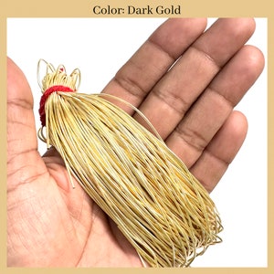 May include: A bundle of dark gold wire, tied with a red string, is held in a hand. The wire is thin and shiny, and it is likely used for jewelry making.