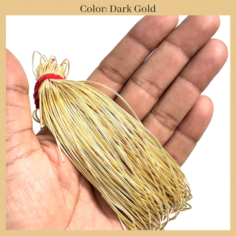 May include: A bundle of dark gold wire, tied with a red string, is held in a hand. The wire is thin and shiny, and it is likely used for jewelry making.