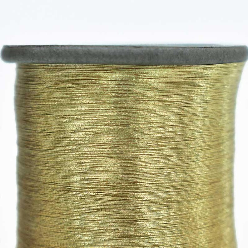 May include: A spool of gold metallic thread. The thread is wound tightly around the spool and has a shiny, metallic finish.