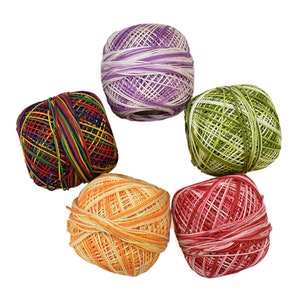 May include: A collection of five colorful yarn balls. The yarn balls are in various colors, including purple, green, red, orange, and a rainbow mix. The yarn is tightly wound and appears to be cotton or a similar fiber, suitable for knitting or crochet projects.