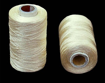 Puede incluir: Dos carretes de hilo de color crema, enrollados firmemente en carretes de cartón.