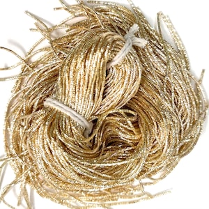 Op de afbeelding: Een bundel gouden metallic koord, gebonden met wit touw. Het koord is glanzend en heeft een lichte glans.