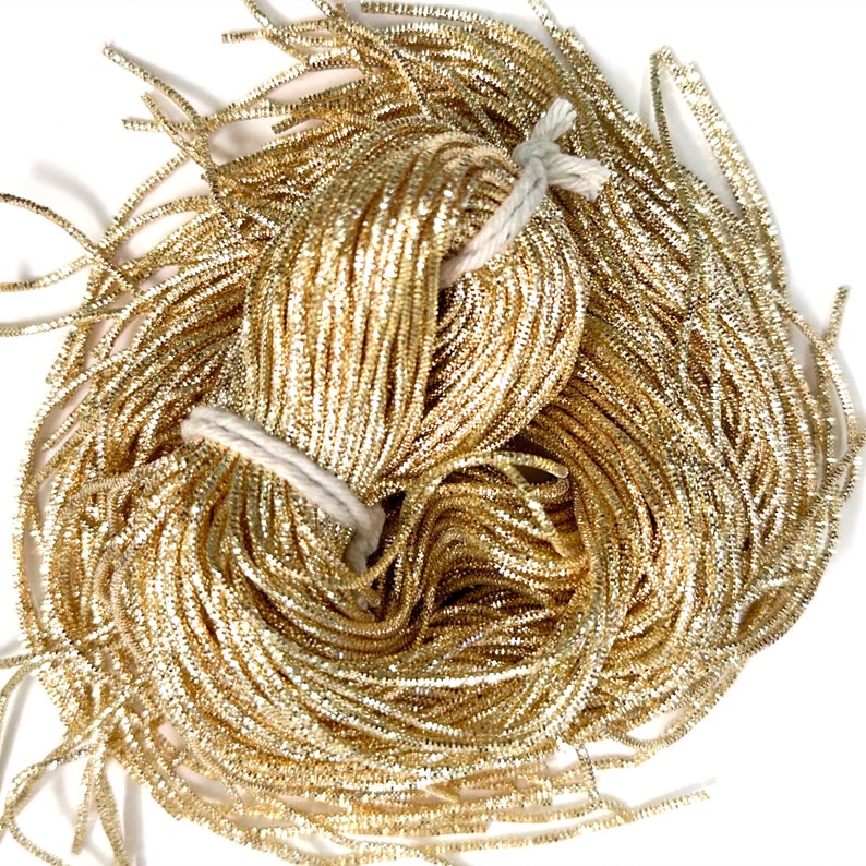 May include: A bundle of gold metallic cord, tied with white string. The cord is shiny and has a slight sparkle.
