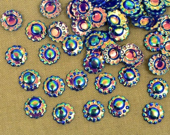 Op de afbeelding: Een strooiing van regenboogkleurige, ronde knopen in blauw en paars met een gegolfde rand. De knopen hebben een glanzende, metallic afwerking.