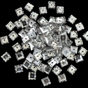 May include: A large pile of silver square-shaped rhinestones with a hole in the center of each rhinestone.