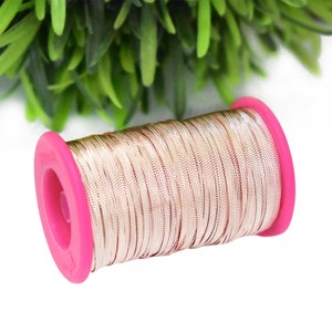 May include: A spool of gold metallic thread wound around a pink plastic bobbin. The thread is shiny and has a subtle texture.