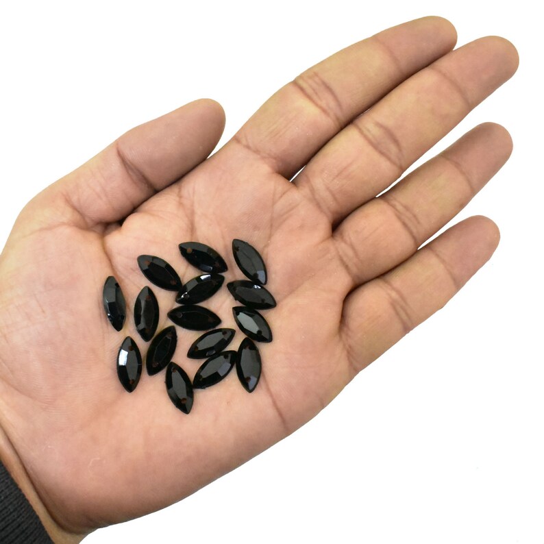 K&ouml;nnte beinhalten: Eine Sammlung schwarzer, marquisef&ouml;rmiger Strasssteine in einer Hand. Die Strasssteine sind facettiert und haben eine gl&auml;nzende Oberfl&auml;che.
