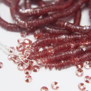 May include: A strand of red iridescent sequins, with a pile of loose red iridescent sequins scattered around it.