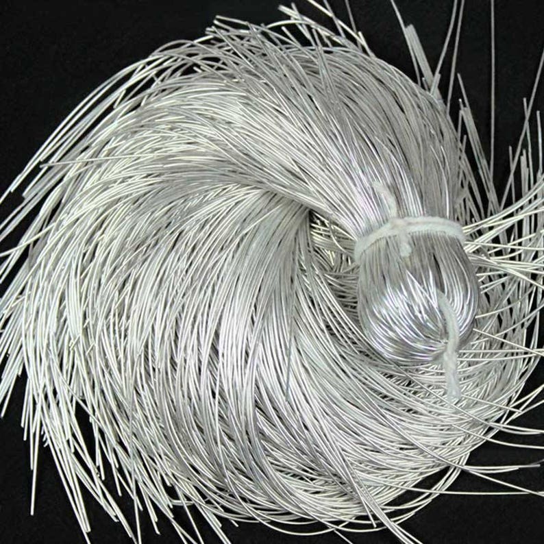 May include: A bundle of silver-colored wire, tightly bound in the center with a white string. The wires are thin and flexible, radiating outwards from the center. The background is a solid black.