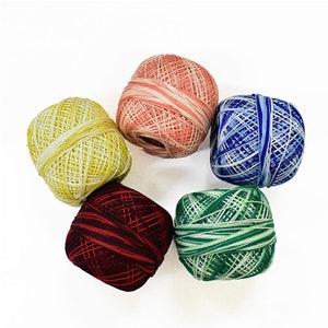 May include: Six colorful balls of crochet thread arranged in a circular pattern. The thread colors include yellow, coral, blue, green, and burgundy. Each ball is tightly wound, showcasing the texture and variety of the thread.