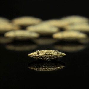 May include: A single gold-coloured, textured, oval-shaped button with a reflective surface.