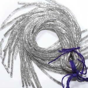 Op de afbeelding: Een bundel zilveren metallic trim, gebonden met een paarse string. De trim is gemaakt van kleine, glanzende, metalen vierkanten.