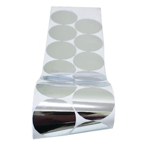 Może przedstawiać: Rolkę srebrnych okrągłych naklejek. Naklejki są ułożone w rzędach na białym podkładzie.