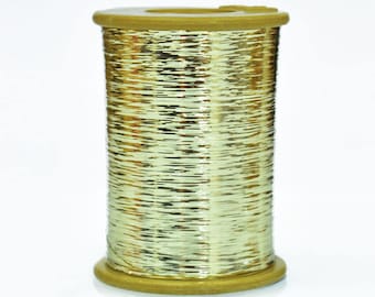 May include: A spool of gold metallic thread. The thread is wound around a brown plastic spool.