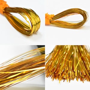 May include: A spool of gold metallic thread, perfect for crafting and decorating. The thread is thin and shiny, and it is wound around a spool with a bright orange center.