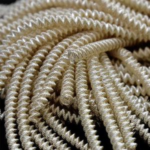 May include: A close-up of a pile of silver-colored, coiled wire. The wire is tightly wound and has a smooth, shiny finish.