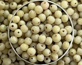 May include: A close-up of a bowl filled with off-white round beads. The beads are smooth and have a slightly iridescent sheen.
