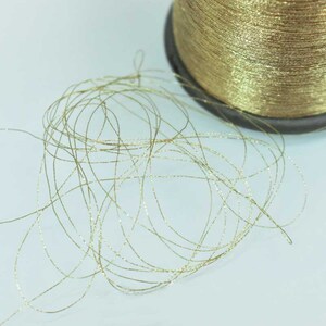 May include: A spool of gold metallic thread with a slight sheen. The thread is unwound and scattered on a white surface.