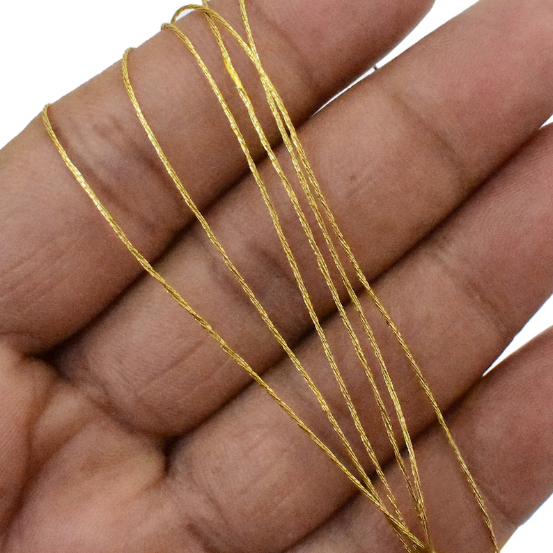 May include: A close-up of multiple strands of gold-colored metallic cord. The cord is thin and has a slightly textured surface.