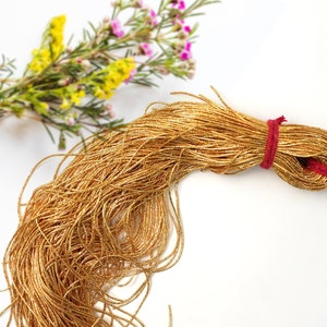 May include: A spool of gold metallic thread, tied with a red string. The thread is loose and flowing, creating a soft, textured look.